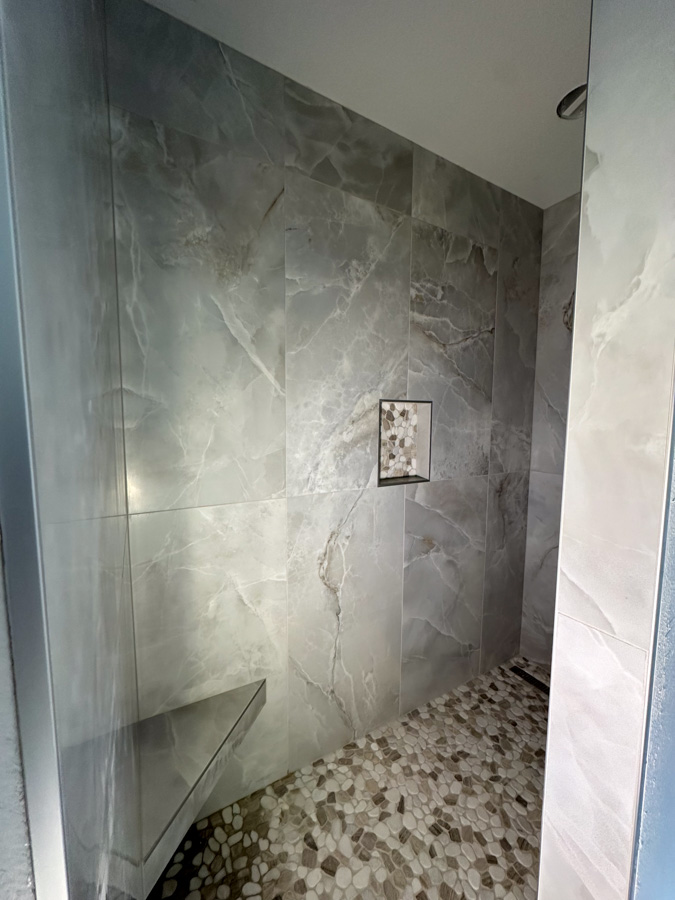 Bathroom remodel in Salmon Creek, WA featuring marble-look wall tile, travertine-style floor tile, dark wood vanity, and modern fixtures.